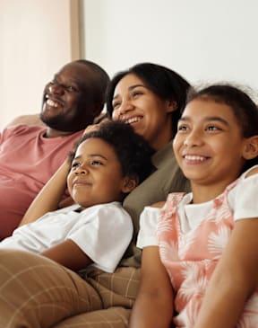 A family of four is sitting together on a couch.