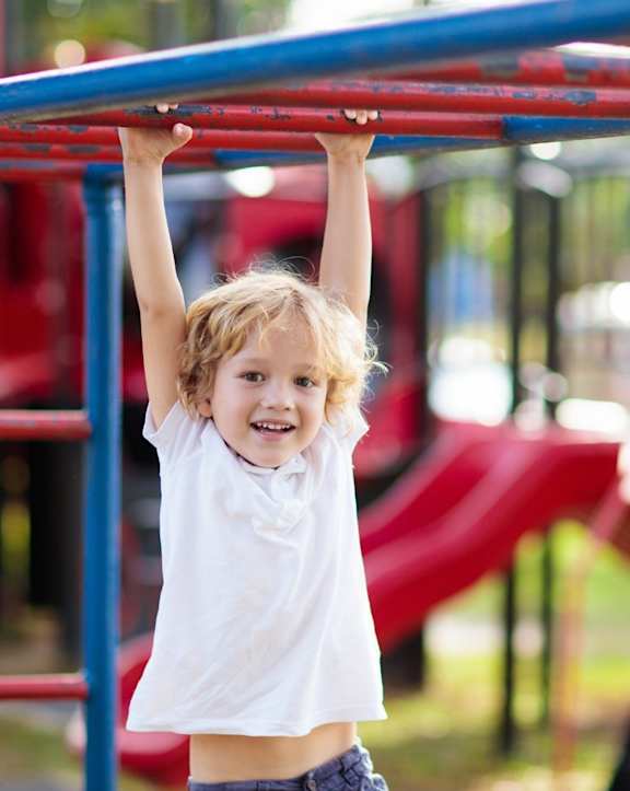 A young child is hanging from a playground bar.