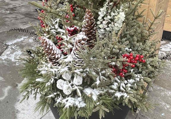 A large pot of Christmas decorations sits on a sidewalk.
