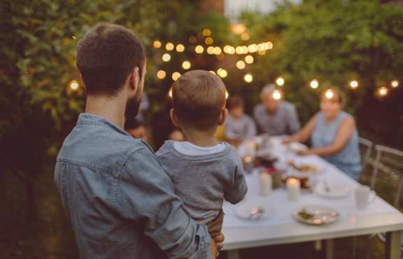 A man holding a child at a dinner table with lights in the background.