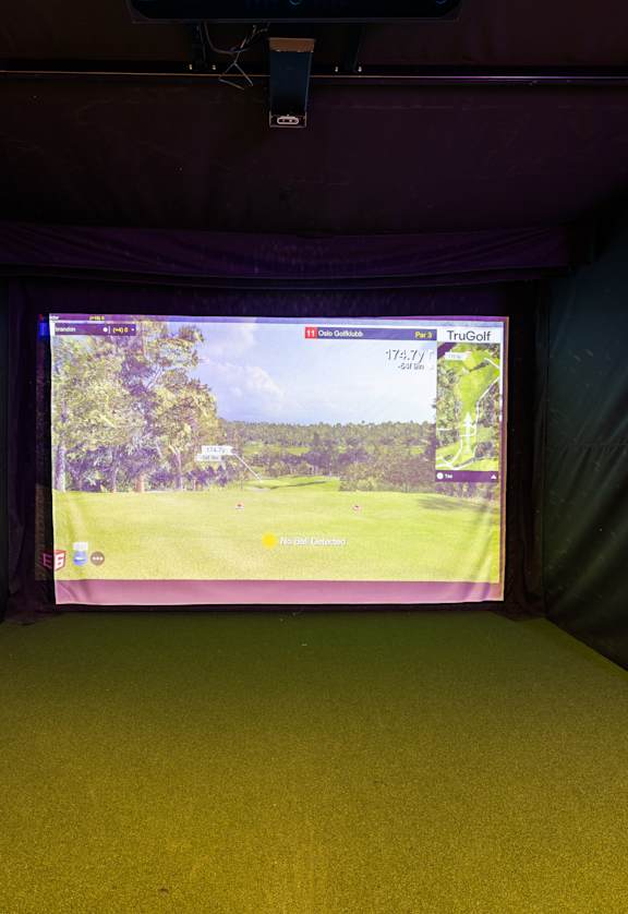 A screen in a dark room shows a golf course.