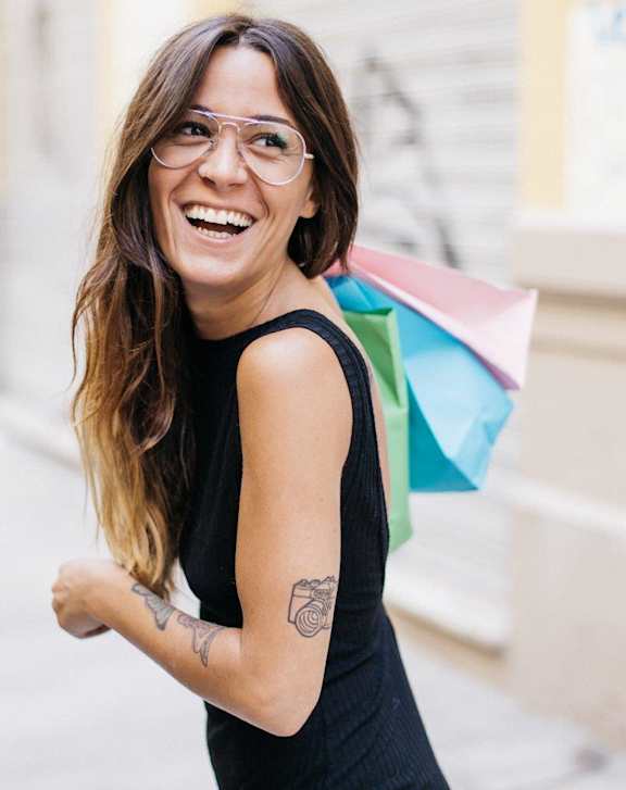 A woman with glasses and a tattoo on her arm is smiling.