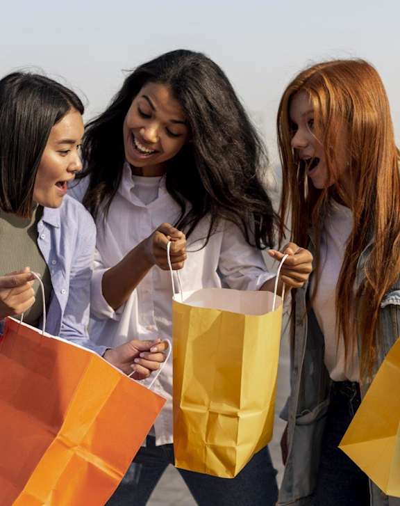 Three women are holding shopping bags and appear to be happy.