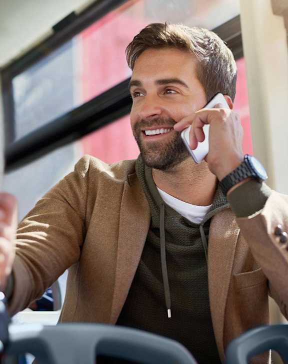 A man in a brown jacket is talking on a white phone.