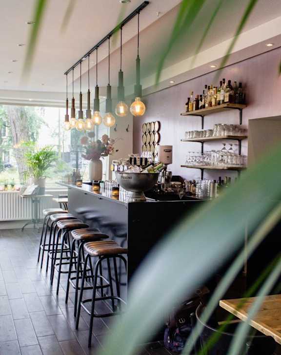 A bar with a black counter and stools with a person behind the counter.
