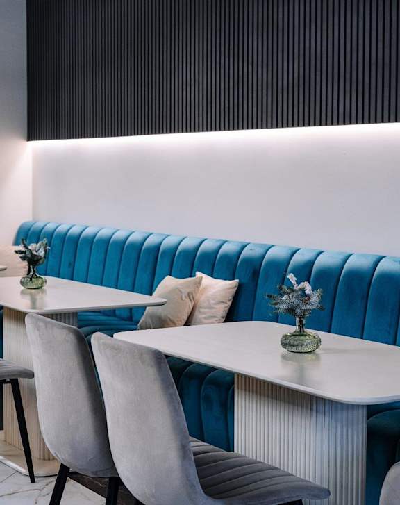 A blue booth with a white table and grey chairs.