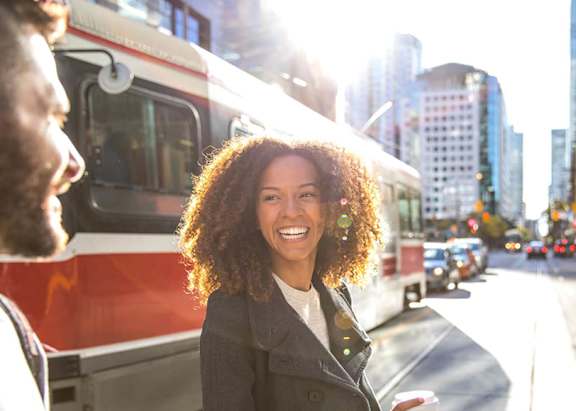 A woman with curly hair is standing on the sidewalk.