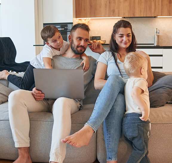 A family of four is sitting on a couch with a laptop.