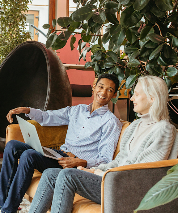 A man and a woman are sitting on a couch with a laptop on the man's lap.