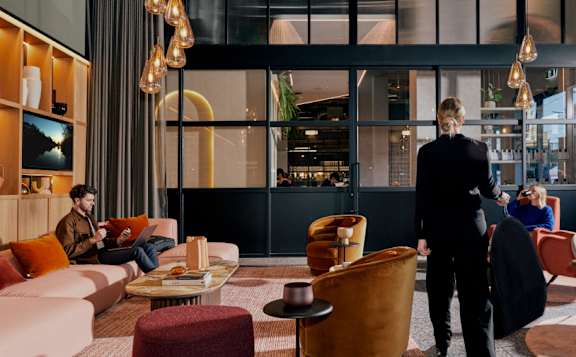 A woman in a black suit walks through a modern lounge area.