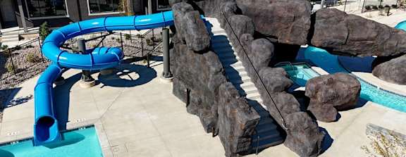 A blue water slide in a pool surrounded by rocks.