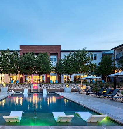 A swimming pool surrounded by lounge chairs and umbrellas in a residential area.