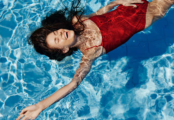 A woman in a red dress is floating in a pool.
