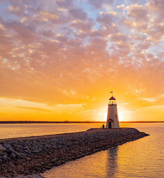 A lighthouse stands on a rocky pier in the middle of the ocean.