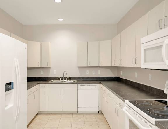 A white kitchen with a refrigerator on the left.