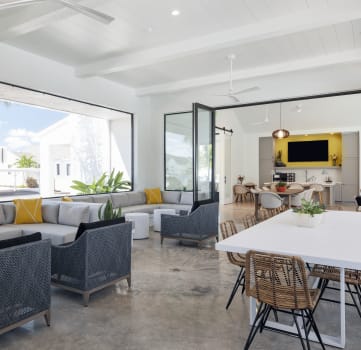 an open concept living room and dining area with a white dining table and rattan chairs