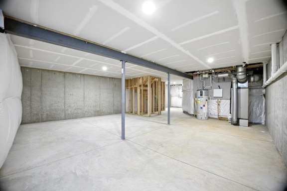 A spacious unfinished room with a concrete floor and walls, and a ceiling with exposed ductwork.