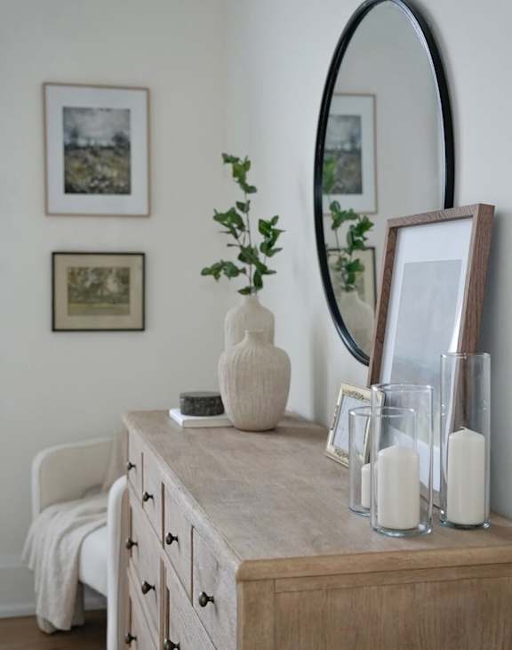 A white vase sits on a wooden dresser next to a mirror and candles.