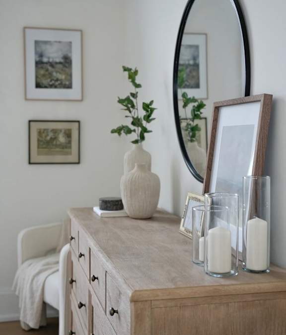 A white vase sits on a wooden dresser next to a mirror and candles.