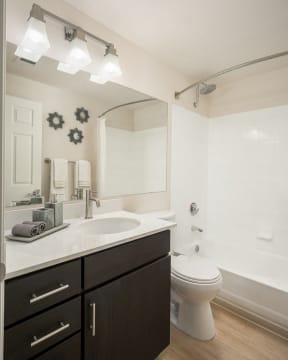 Bathroom with light faux wood floors, brown cabinets, white quartz cabinets and tub/shower