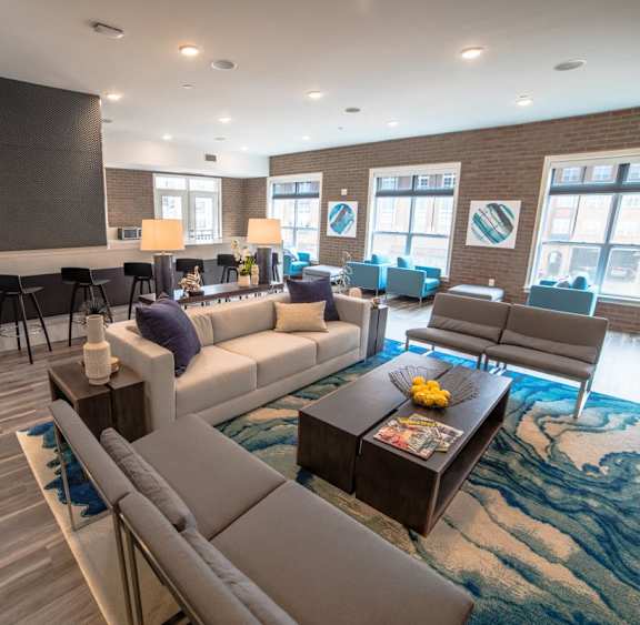 A living room with a white sofa, grey armchair, and a coffee table with a bowl of fruit on it at The Foundry Apartments , South Bend, IN, 46617