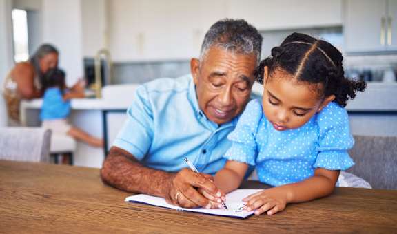 an older man sitting at a table with a young girl writing on a piece of paper