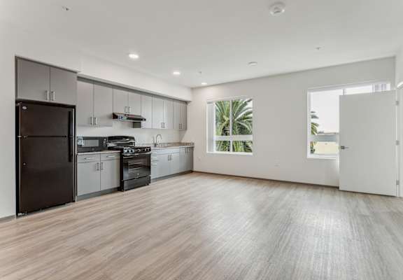 an empty kitchen with white walls and wood floors and a black refrigerator