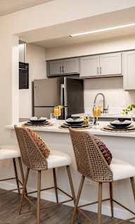 A kitchen with a white countertop and brown chairs.