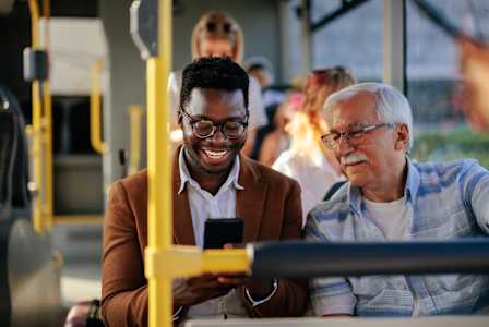 Two men are sitting on a bus looking at a smartphone.