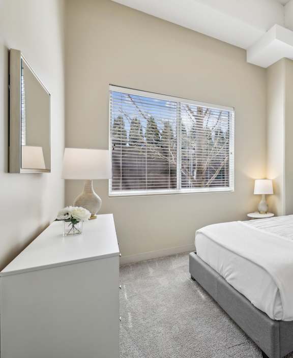 A bedroom with a large bed and a window with blinds.
