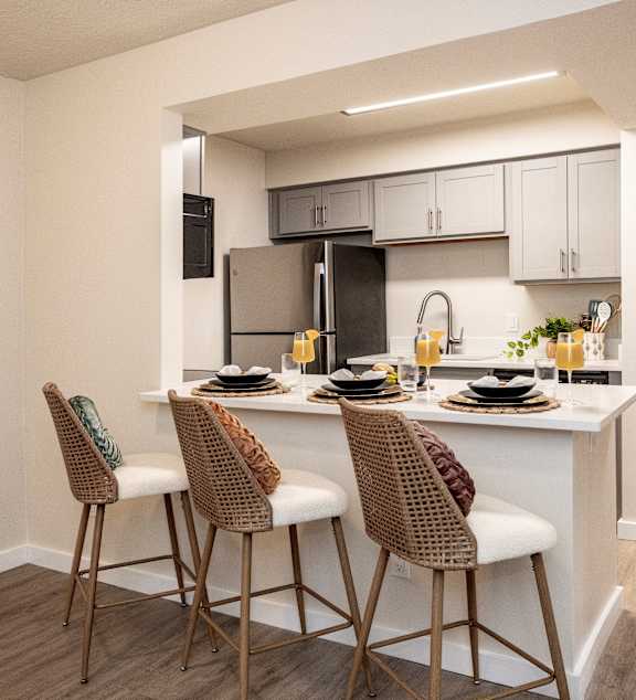 A kitchen with a white countertop and brown chairs.