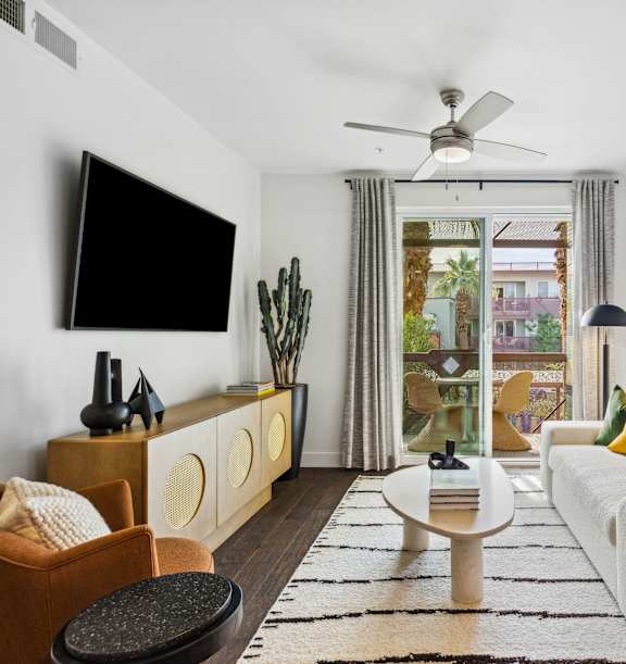 A living room with a white couch, a black table, and a flat screen TV mounted on the wall.