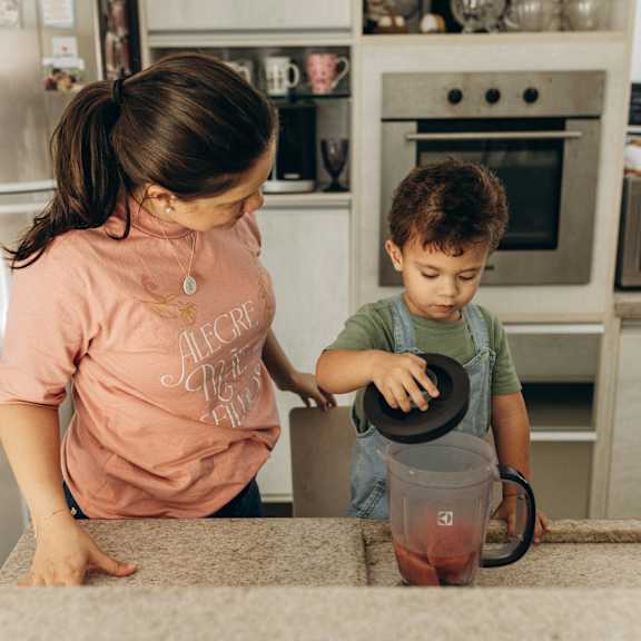 A woman and a child are in a kitchen, with the child holding a blender.
