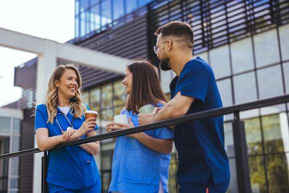 Three people in blue scrubs are standing on a balcony.