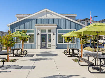A building with a blue and white exterior has a covered patio with tables and chairs.