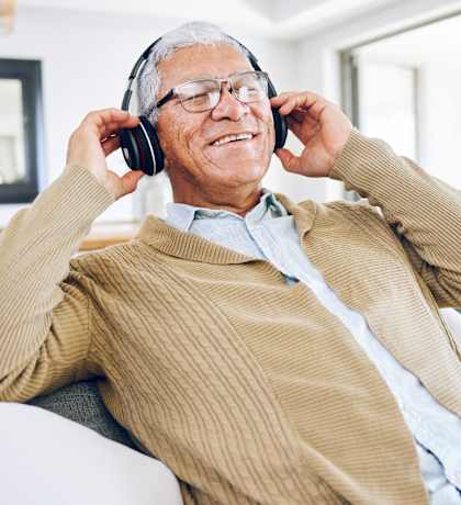 an older man sitting on a couch talking on two headphones