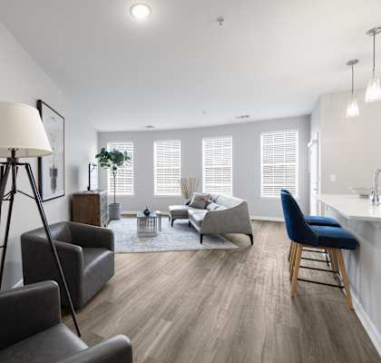 A well-lit living room with a grey sofa, a black chair, and a wooden floor.