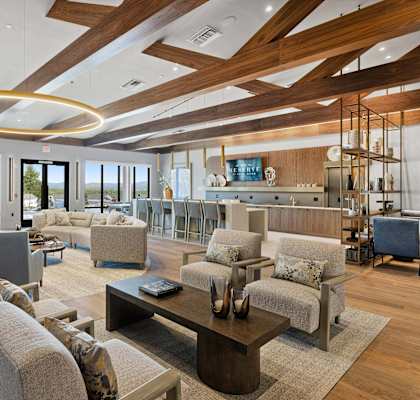 A modern living room with a large circular light fixture and a view of the outdoors through the windows. at The Reserve at Pearl River Apartments, New York