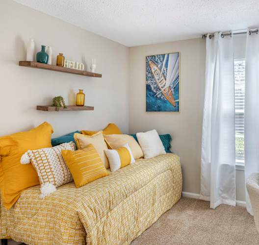 A bedroom with a yellow bed and a painting on the wall.