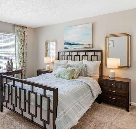 A bedroom with a large bed, a blue chair, a desk, and a painting on the wall.