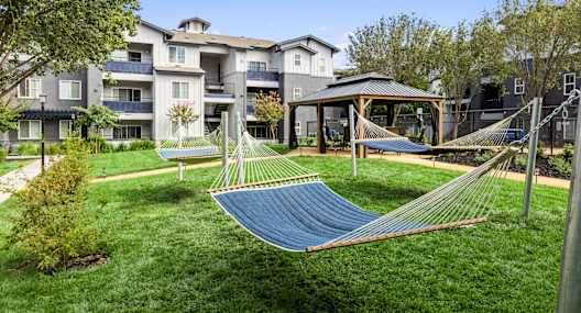 a yard with hammocks and a gazebo in front of an apartment