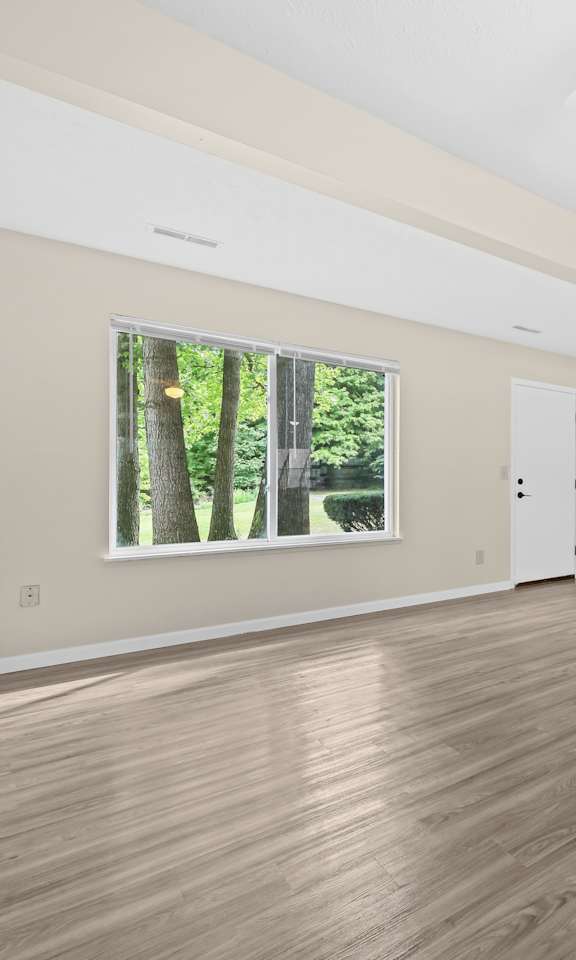 A room with wooden flooring and a window showing trees outside.
