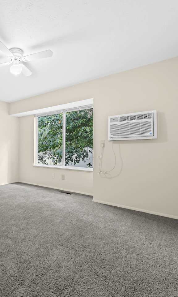 A room with a ceiling fan and a window with an air conditioner unit on the wall.