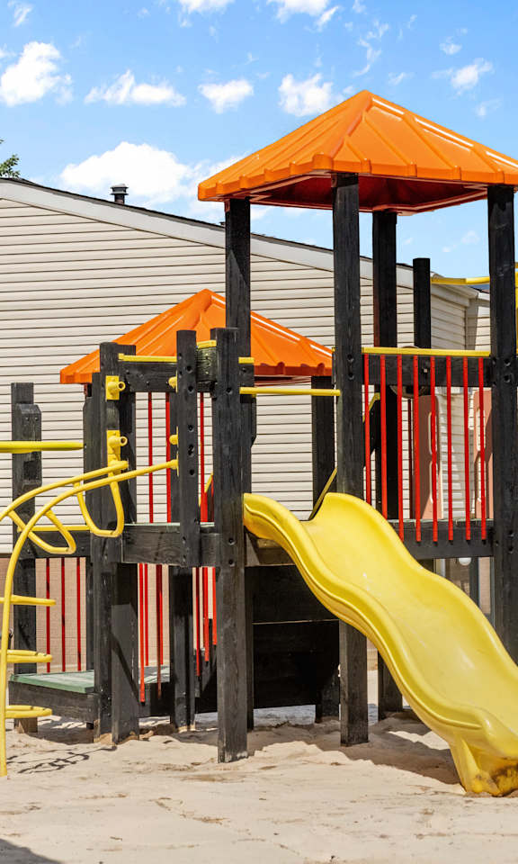 A playground with a yellow slide and an orange roofed structure.