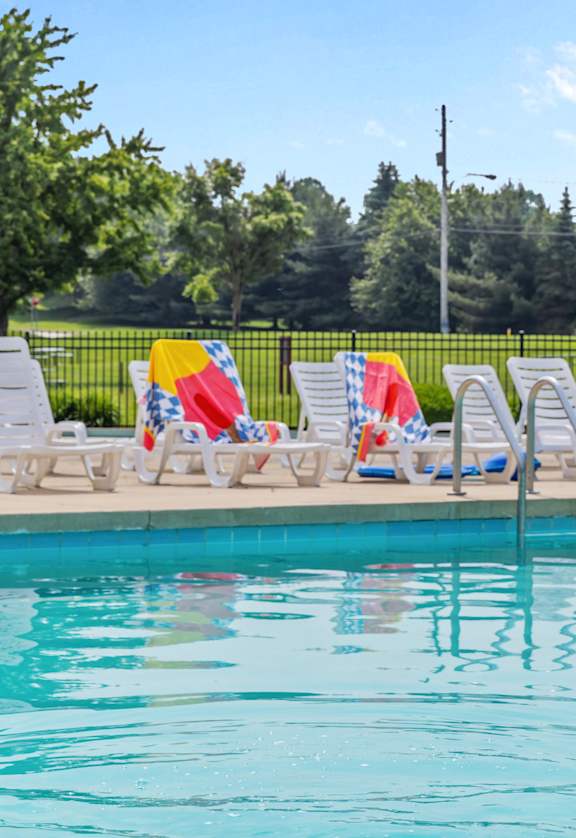 A pool with a blue and pink ball and chairs around it.