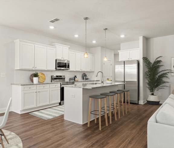 an open kitchen and living room with white cabinets and a bar with stools