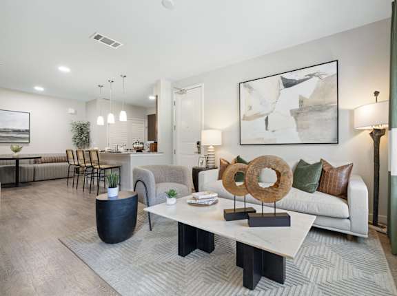 A modern living room with a white sofa, a coffee table, and a large abstract painting on the wall.