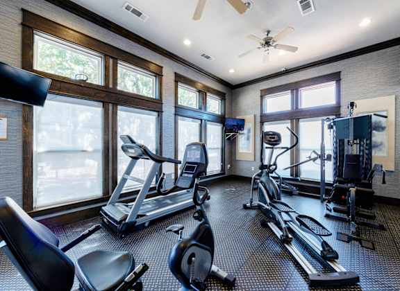 A spacious gym with treadmills, elliptical machines, and a ceiling fan.