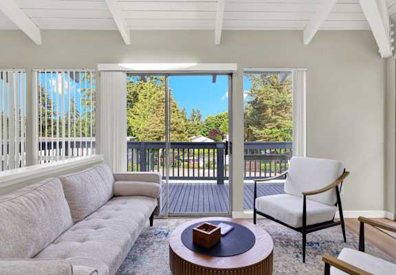 A white couch sits in a sunny room with a view of a deck.