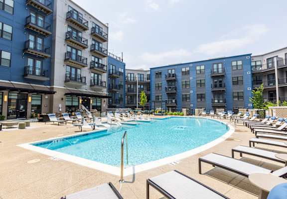 a large swimming pool with chaise lounge chairs and a building in the background